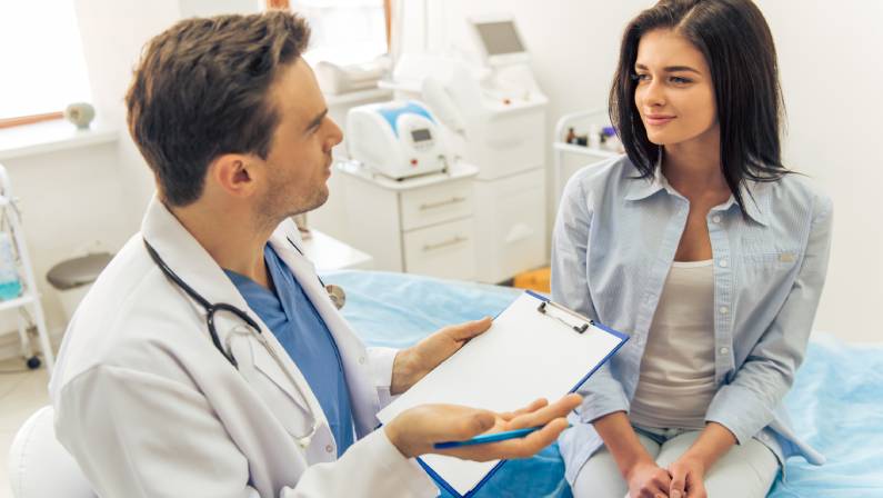 Male Doctor is talking with young female patient about Miami Thong Lift Procedure and making notes