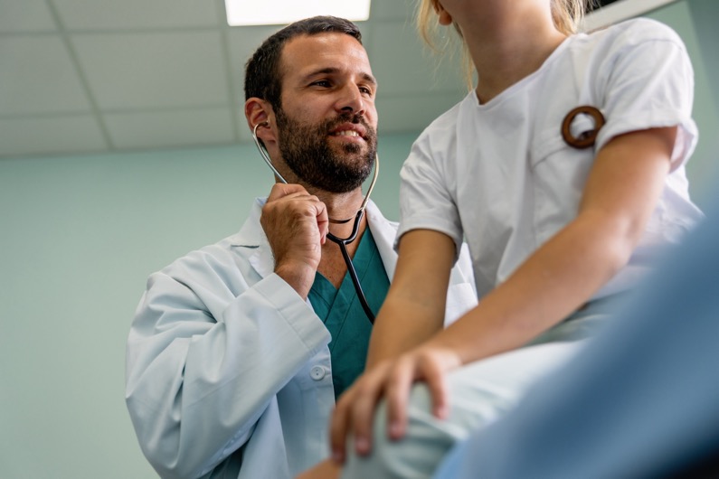 Doctor giving checkup with stethoscope to young girl in exam room
