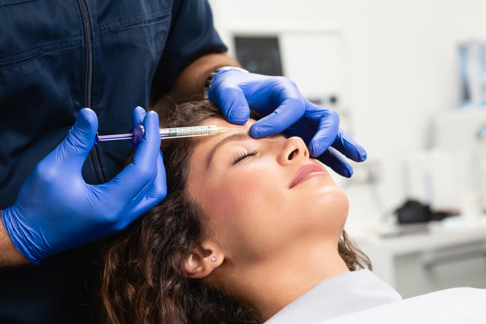 Close up of beautician expert's hands injecting botox in female forehead.