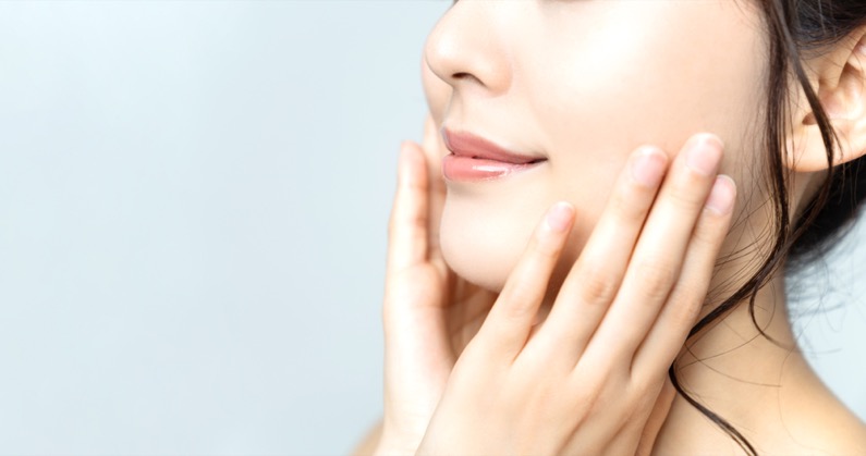 Close-up of a woman touching her smooth jawline after Chin Augmentation, showing a defined and balanced facial profile.