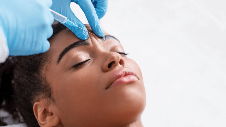 Young African woman receiving botox injection in interbrow zone at beauty clinic.