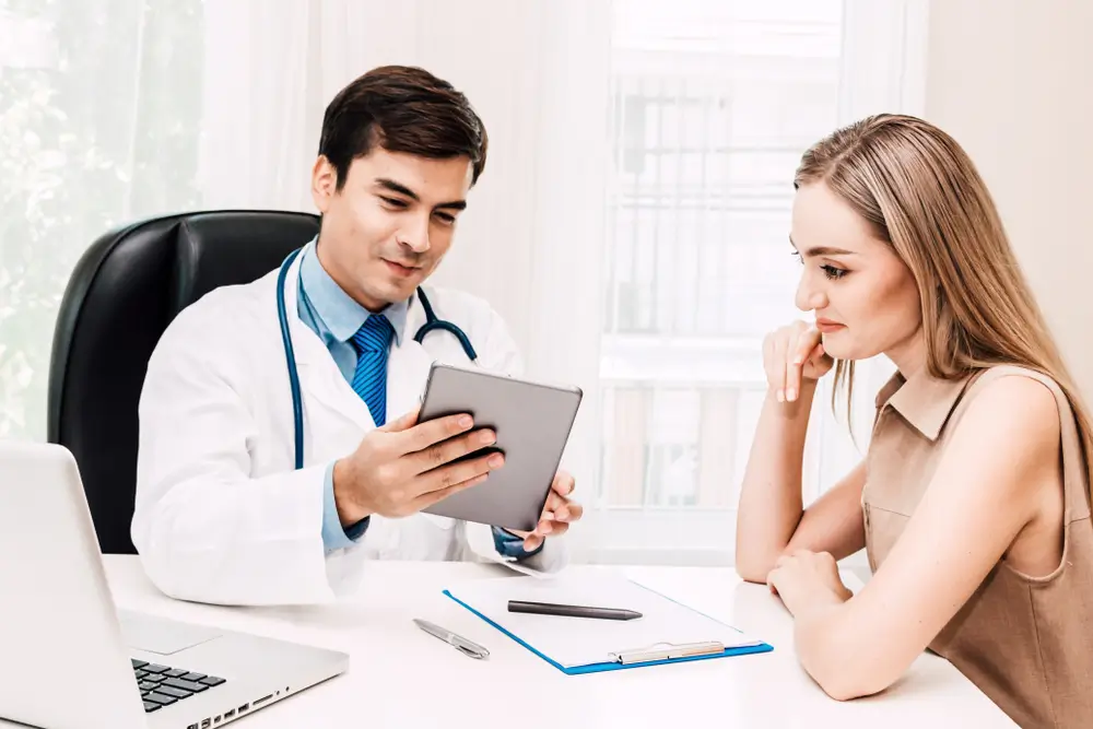 Doctor discussing and consulting with female patient on doctors table in hospital.