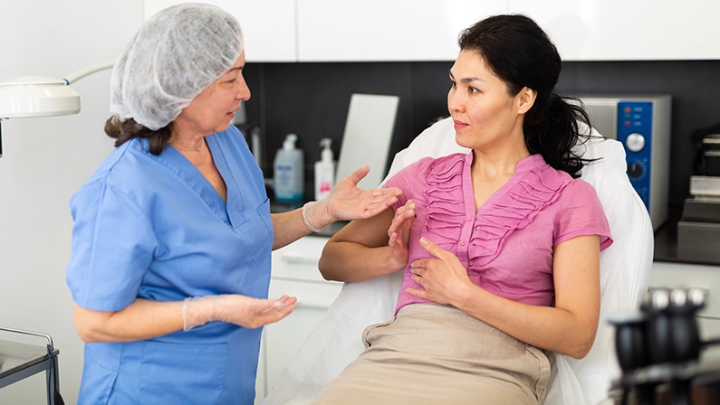Plastic surgeon and woman discussing procedure of breast augmentation during consultation at clinic