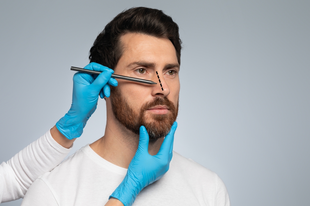 Doctor in protective gloves drawing marks on man's nose for cosmetic surgery operation