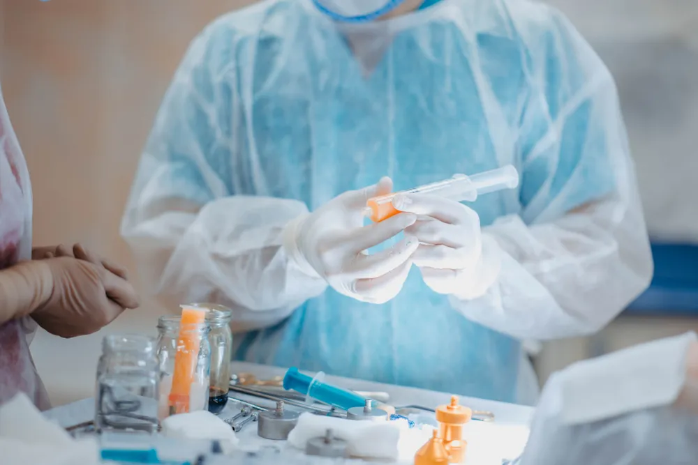 Surgeons preparing medical instruments and syringes for facial procedure comparing fat grafting vs. fillers results.