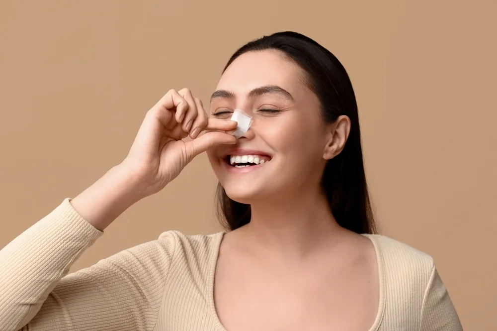 Smiling woman with bandage on her nose after rhinoplasty, showing early healing and minimal rhinoplasty scarring.