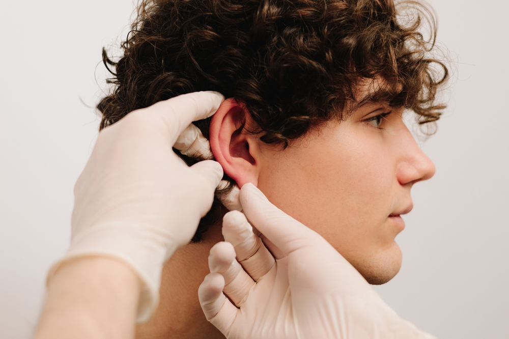 surgeon inspecting young man's ear for otoplasty surgery