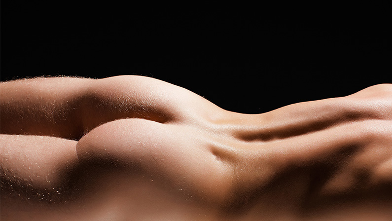 Artistic close-up of a sculpted male back and hips highlighting smooth contours after cosmetic enhancement for man with BBL.