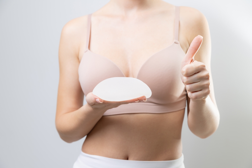 Female holding silicone breast implant and giving thumbs up gesture, test quality.