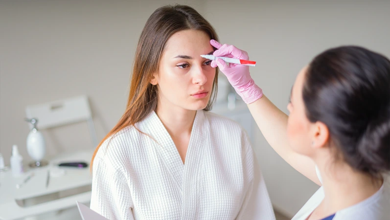 Cosmetologist ready to paint lines with marker on patient face