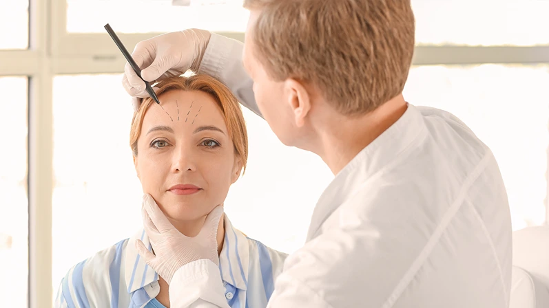 Plastic surgeon applying marks on woman's face in clinic